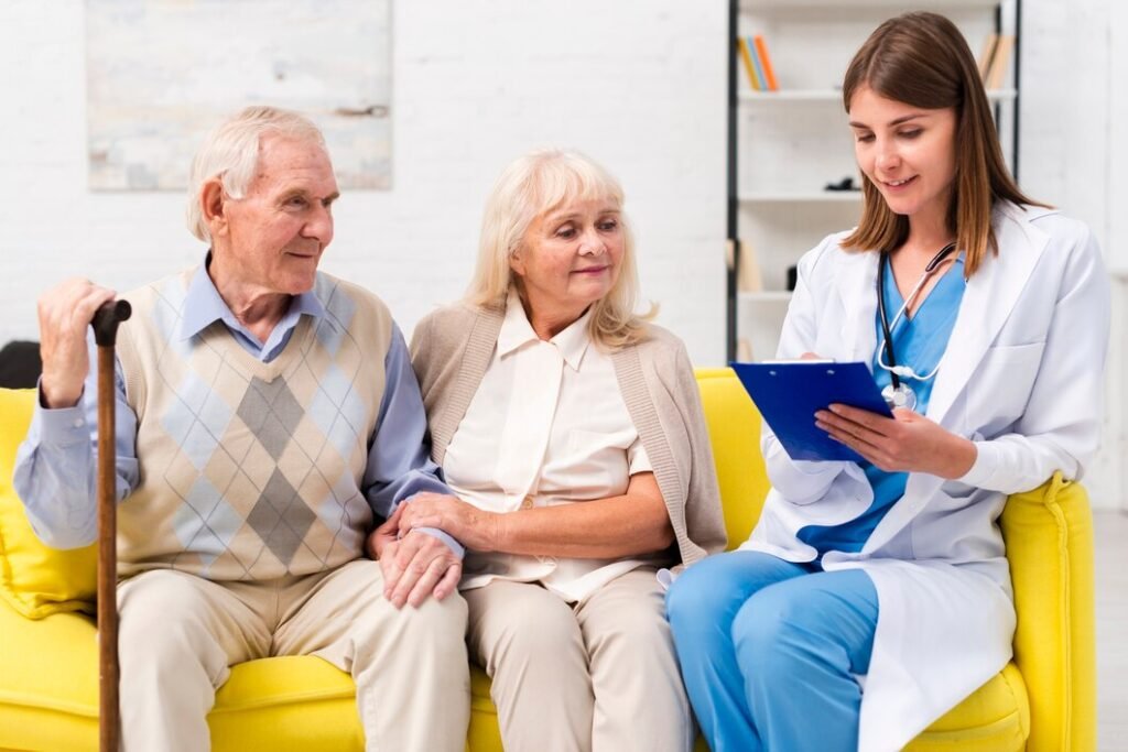 Photo of a nurse sitting with an elderly man and woman on a sofa while discussing care in a home or clinical setting. Image used by a medical clinic in San Bernardino to represent senior care and supportive healthcare services